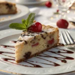 Elegant slice of cherry chip cake garnished with mint and chocolate sauce on a fine china dish.